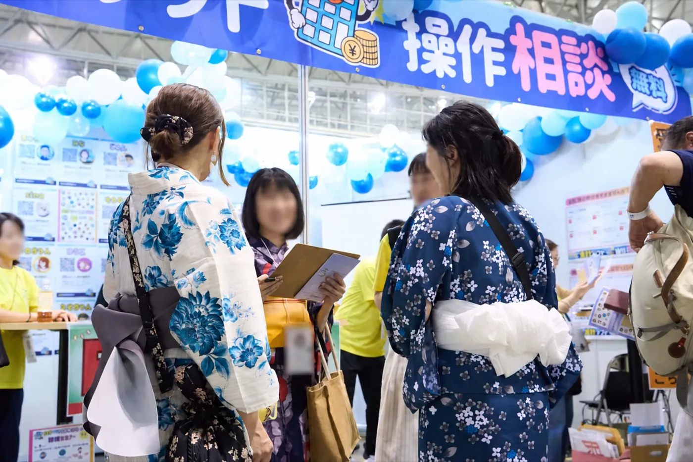 青い風船で飾られた操作相談ブースで来場者に説明する出店者
